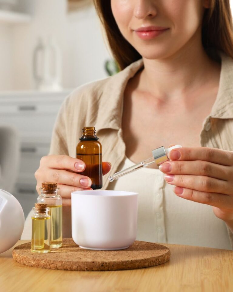 Mulher em ambiente minimalista utilizando óleos essenciais em difusor elétrico, estética clean e sofisticada de bem-estar.