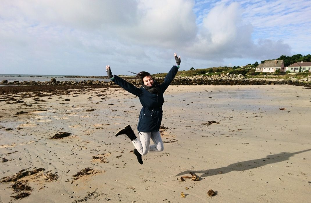 Fundadora da Swaminah saltando de alegria em uma praia na Irlanda, celebrando a liberdade e o alívio encontrados através da natureza