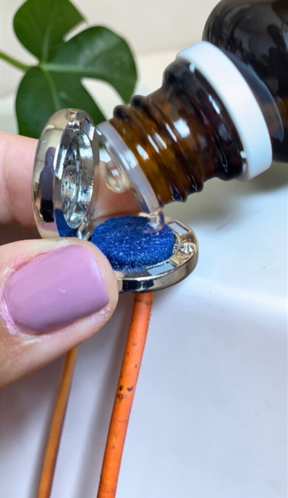 Detalhe macro de pingente Swaminah aberto recebendo gota de óleo essencial dōTERRA.